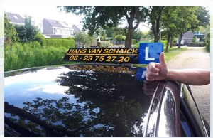 De lesauto van Autorijschool Hans van Schaick met daklicht en L-plaat op een weg bij Makkum